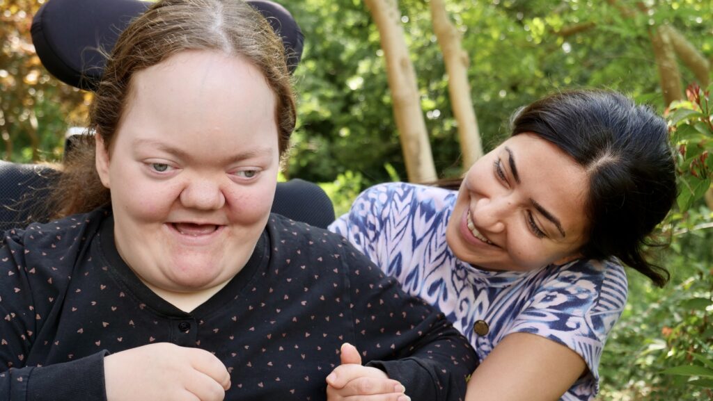Anna, en kørestolsbundet kvinde med bolig på Udsigten, forbinder sig glad med en medarbejder.